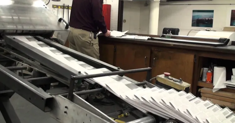 A newspaper press with lots of newspapers being printed.