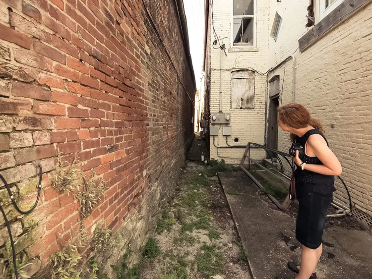 Woman with camera in her hand looking down a narrow alleyway.