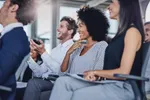 Diverse professionals smiling and applauding during a business presentation in a modern office setting.